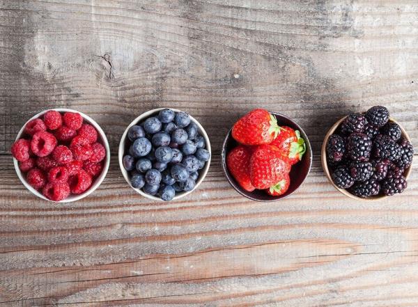 Berries lined up in bowls on wood surface